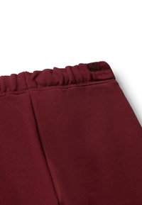 Bordeaux joggers met een geplooide tailleband, een soepele textuur en een klein logotag. De stof lijkt zacht en rekbaar te zijn.