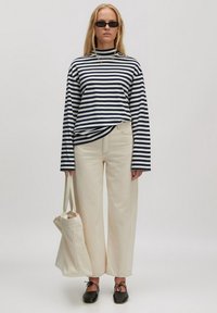 Gestreiftes Langarmoberteil in Marineblau und Weiß, cremefarbene weit geschnittene Hose, schwarze Slippers und eine Stofftasche. Minimalistisches Design mit klaren Linien.