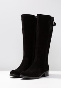 Bottes hautes noires en daim souple. Dotées d'une fermeture éclair latérale et d'un petit talon. Conçues avec des lignes épurées et des accents de quincaillerie minimalistes.