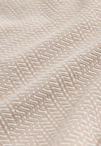 Barna árnyalatú texturált szövet ismétlődő geometriai mintával; cikkcakk vonalakkal és apró fehér pöttyökkel a részletek gazdagításához.