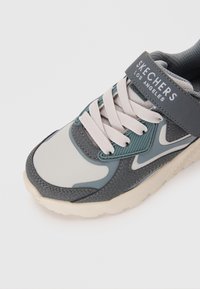 Skechers Sneaker mit einem grauen und blauen synthetischen Obermaterial, ausgestattet mit Mesh-Akzenten, weißen Schnürsenkeln und einem gepolsterten Kragen für zusätzlichen Komfort.