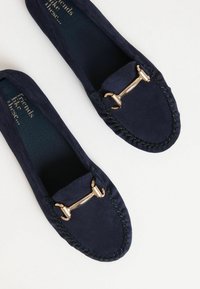 Mocassini in suede blu navy presentano un dettaglio in metallo dorato e una cucitura decorativa. L'interno è trapuntato per comfort e supporto.
