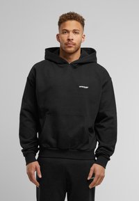 Black cotton hoodie featuring a kangaroo pocket, drawstring hood, and small white logo on the chest; ribbed hem and cuffs.