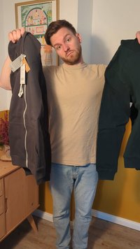 Divi zip-up kapuces tur personā: kreisajā pusē tumši pelēks, labajā pusē tumši zaļš. Abiem ir ribotas piedurknes un vienkāršs dizains.