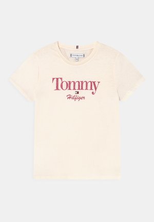 Kremfarvet T-shirt med korte ærmer med "Tommy Hilfiger"-logo i rød tekst og et lille flag-symbol centreret foran.