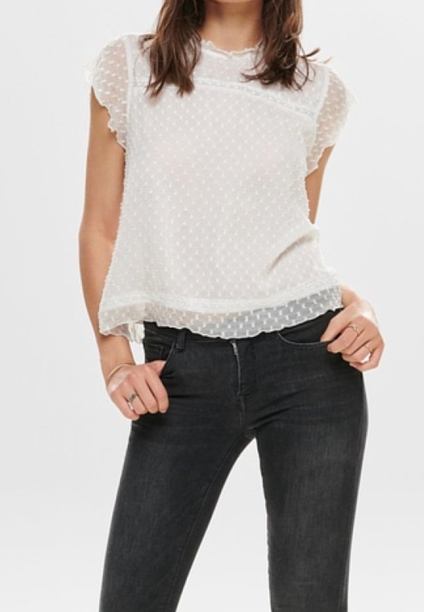 Blusa blanca con lunares, de mangas cortas con volantes, escote ondulado y superposición transparente, combinada con jeans oscuros.