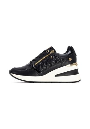 Zapatilla negra de cuero con textura acolchada, detalle de cremallera dorada y suela de cuña. Media suela blanca con acento negro. Acabado suave y brillante.