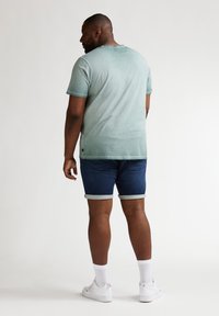 Camiseta de manga corta verde claro con un efecto degradado, combinada con pantalones cortos de mezclilla azul oscuro. Calcetines blancos y zapatillas completan el conjunto.
