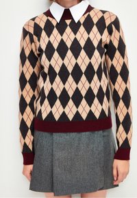 Maglione a motivo argyle beige, nero e bordeaux con colletto bianco, abbinato a una gonna in tweed grigia dal design aderente.