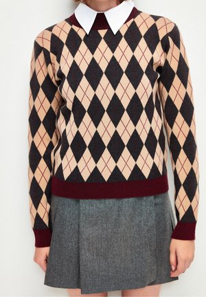 Pull à motif argyle en beige, noir et bordeaux avec un col blanc, associé à une jupe en tweed gris au design ajusté.