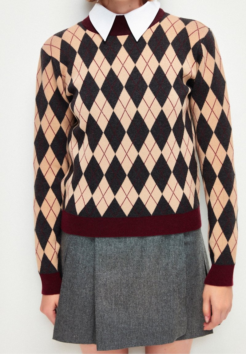 Maglione a motivo argyle beige, nero e bordeaux con colletto bianco, abbinato a una gonna in tweed grigia dal design aderente.