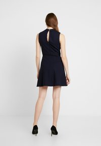 Námořnická modrá bezramínková šaty s vypasovaným korzetem, krajkovým lemem a klíčkovým výstřihem na zádech. Rozšířená sukně se scalloped lemováním. Nosit s černými vysokými podpatky.