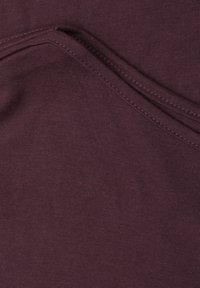 Gros plan d’un tissu violet foncé plié avec une double surpiqûre visible le long du pli, montrant la texture et les détails de la couture.