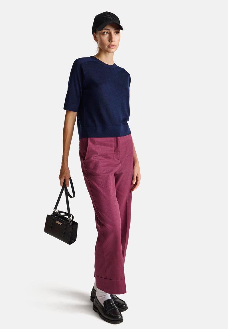 Granatowy sweter z dzianiny, burgundowe spodnie o szerokich nogawkach, czarne mokasyny z białymi skarpetkami, czarna torebka i czapka z logo.