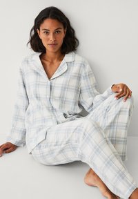 Geruite pyjama set met een lichtblauw en wit ruitpatroon, gemaakt van zachte stof met lange mouwen en loszittende broeken.