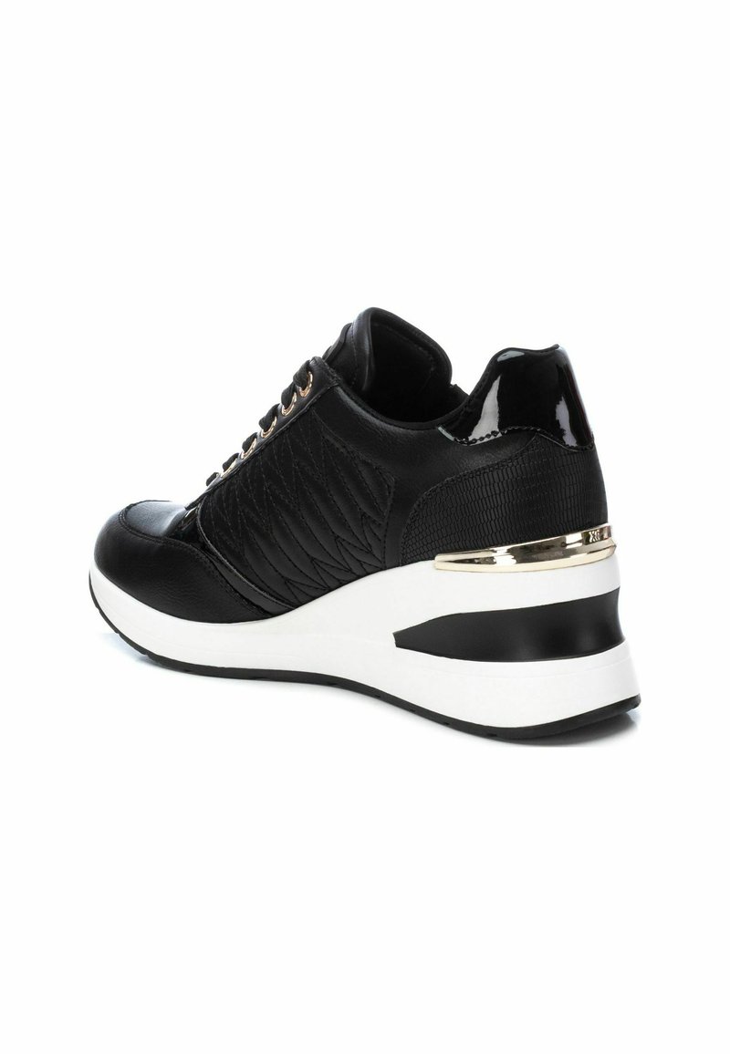 Zapatilla negra con textura acolchada, acentos brillantes, cordones en la parte delantera y una suela wedge blanca con una franja negra y dorada.