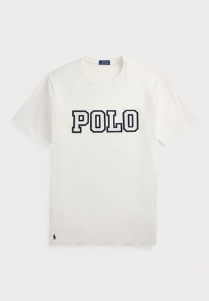 Balta kokvilnas T-kreklu ar īsām piedurknēm, uz kura priekšpuses ir prints "POLO" tumši zilā krāsā un mazs tumši zilais logo apakšējā kreisajā stūrī.