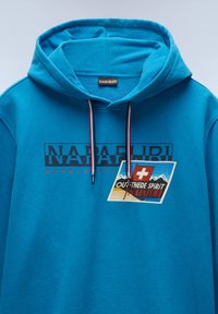 Felpa con cappuccio turchese realizzata in tessuto morbido, con un logo grafico, righe sul cordino e un'etichetta rettangolare con immagini di montagne.