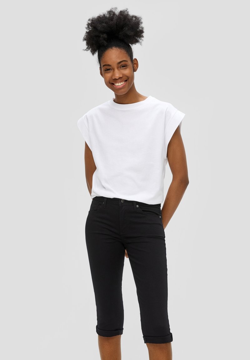 T-shirt en coton blanc à manches courtes roulées associé à un jean noir ajusté jusqu'aux genoux, avec un design cinq poches classique.