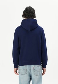 Navy blue hoodie with a soft texture, featuring a large hood and ribbed cuffs, paired with light blue denim jeans. Rear view shown.