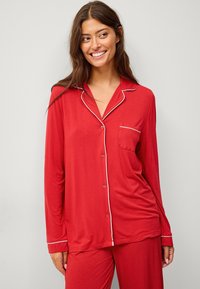 Rode pyjama set gemaakt van zachte stof. De top heeft een kraag, lange mouwen en een enkele borstzak met witte piping accenten.