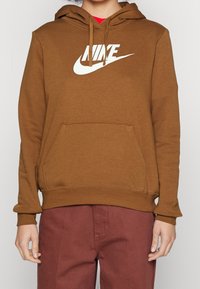 Brun hoodie med känguruficka, med en stor vit Nike-logga på framsidan och justerbar huva med dragsko. Avslappnad passform.