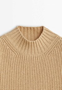 Pull beige en maille avec un col haut côtelé et un motif de point texturé sur le corps et les manches.