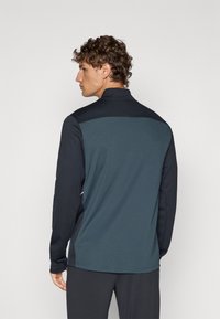 Zwarte en teal sportjas met hoge kraag, lange mouwen en een gestructureerd achterpaneel, ontworpen voor een getailleerde silhouet.