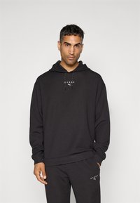 Black hoodie made of soft fabric with a kangaroo pocket, adjustable drawstring, and white "HYROX" and Puma logos on the front.