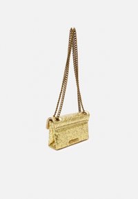 Mała prostokątna torebka z złotym brokatem, z podwójnym złotym łańcuszkiem i zapięciem na klapkę, na jednolitym białym tle.