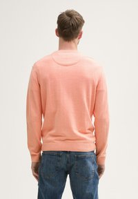 Pullover aus leichtem Pfirsichstrick, mit Rundhalsausschnitt und langen Ärmeln. Kombiniert mit blauen Jeans, was einen lässigen Look betont.