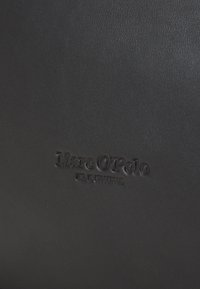 Black leather wallet with a textured finish, featuring an embossed "Marc O’Polo" logo, showcasing a minimalist design.