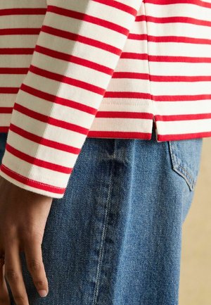 Gestreiftes Langarmoberteil in Rot und Weiß aus Rippstoff, kombiniert mit hellblauen High-Waist-Jeans aus Denim. Mit einem Seitenschlitz am Saum.
