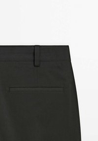 Pantalon noir avec un tissu lisse et texturé, une ceinture fine, une poche arrière et des détails de couture précis.