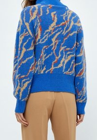 Niebieski, puszysty sweter z wijącym się beżowo-czerwonym wzorem, z prążkowanym dołem i mankietami, zaprojektowany z wysokim kołnierzem.