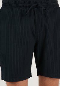 Shorts negri cu nervuri, cu talie elastică și șnur. Prezintă un material texturat cu croială dreaptă, ajungând până la jumătatea coapsei.