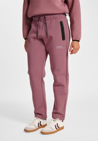 Ljusrosa bomulls-joggingbyxor med dragsko i midjan, sidofickor och en svart dragkedjsficka som detalj. Matchas med vita och bruna sneakers.