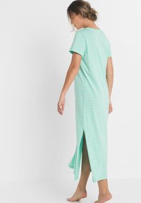 Maxi dress a righe verdi e bianche, maniche corte, fessure laterali per facilità di movimento, realizzato in tessuto leggero.