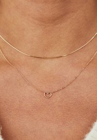 Gold necklaces featuring a thin, smooth chain and a delicate heart pendant; soft, luminous finish against skin.
