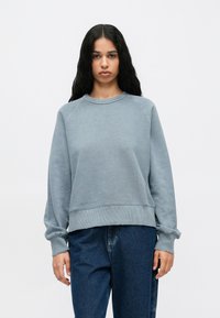 Sudadera azul claro con cuello redondo, mangas raglán y puños acanalados. Hecha de material suave con un corte holgado.