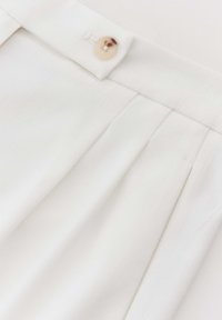 Tissu blanc plissé avec une texture subtile, comportant un seul bouton rond à la taille. Design épuré sans motifs visibles.