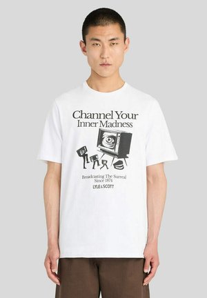 Homme portant un T-shirt blanc avec un graphique noir de télévision vintage et de caméras et texte "Channel Your Inner Madness" et "Broadcasting The Surreal Since 1874."