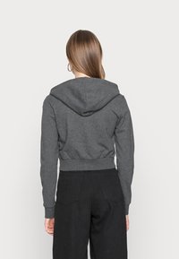 Sudadera gris recortada con capucha con cordón, puños y dobladillo acanalados, hecha de material suave, combinada con pantalones negros de cintura alta.