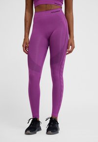 Paarse sportleggings met een hoge tailleband, texturenpatronen en een aansluitend ontwerp, gecombineerd met zwarte sportschoenen.