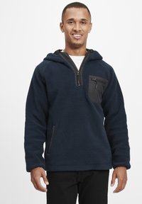 Marineblå fleece pullover hoodie med en sort lynlåslomme på brystet, sidelommer og et tekstureret stof for varme.
