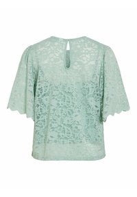 Blouse en dentelle vert clair avec motif floral, manches courtes larges et petite ouverture en forme de goutte d'eau dans le dos de l'encolure.