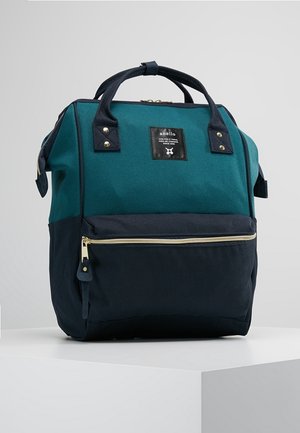Sac à dos rectangulaire bleu sarcelle et noir avec poignées supérieures, poche avant zippée et petite étiquette de marque sur le panneau avant supérieur.