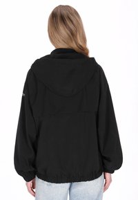 Zwarte, met capuchon uitgeruste jas gemaakt van een lichtgewicht materiaal, met elastische manchetten en een zoom met trekkoord. Gladde textuur met minimale details.