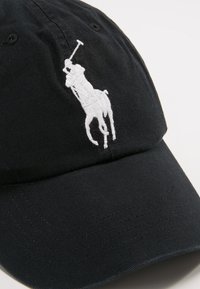 Cappellino da baseball nero in cotone con visiera curva, caratterizzato da un logo di polo ricamato in bianco sulla parte anteriore.