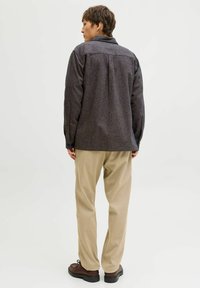 Tumehall teksaga nööbitav särk tekstuurse kangaga, üheosaline seljatükk ja pikad varrukad, kombineeritud beežide pükstega ja pruunide kingadega.